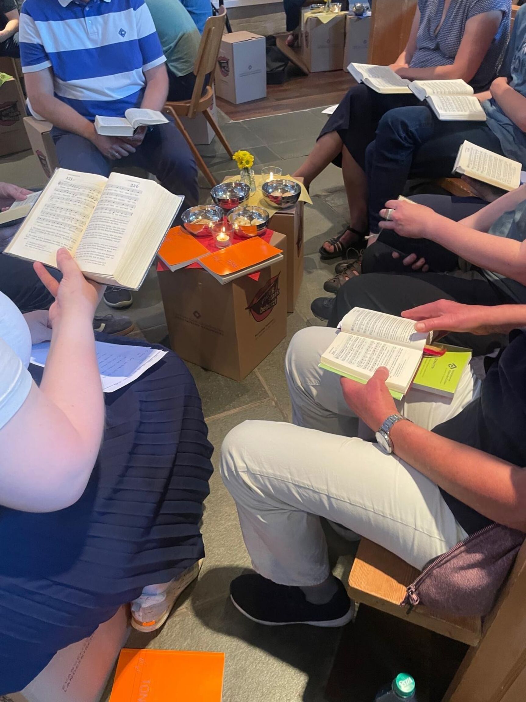 Menschen sitzen auf Kirchentagshocker mit Gesangbüchern und kleinen Beistelltischen im Gottesdienst