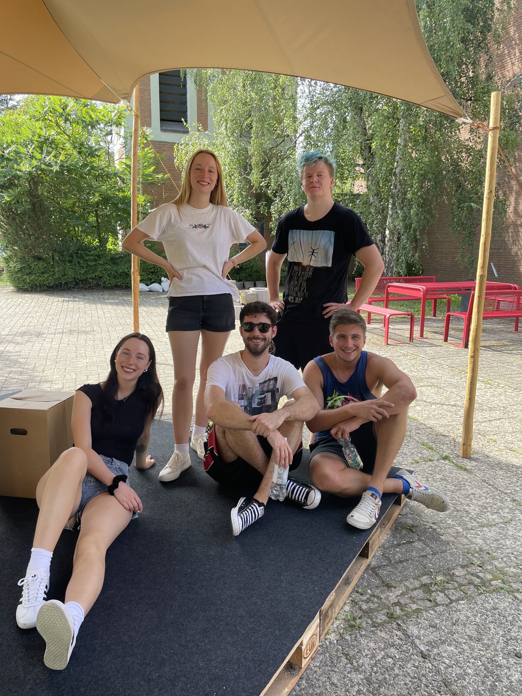 die Punkband Over Your Head auf der Sommer-Bühne unter dem Zelt, aufgestellt zum Foto. eine Frau und ein Mann stehen, eine Frau und zwei Männer sitzen davor auf dem Boden der Bühne