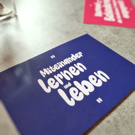blaue Postkarte mit dem Aufdruck "Miteinander lernen zu leben"