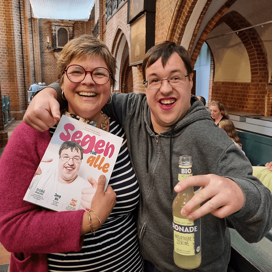 Eine Frau und ein Mann lächeln in die Kamera mit einem Magazin und Limonade in der Hand