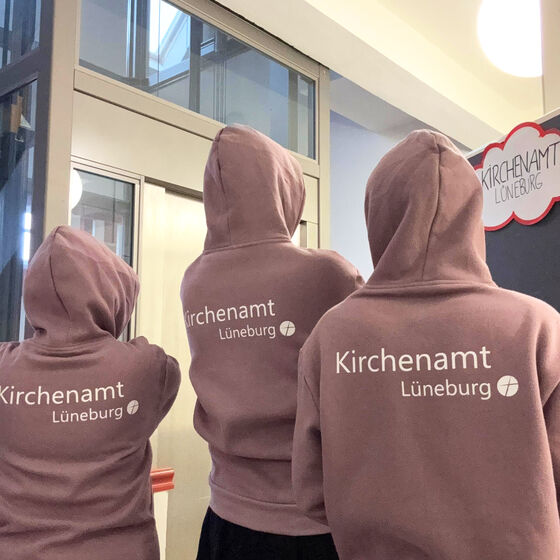 Mitarbeitende zeigen den Aufdruck auf der Pullirückseite: Kirchenamt Lüneburg