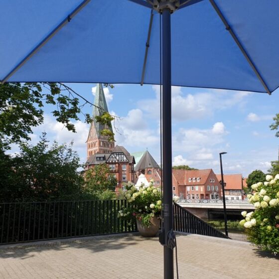 Ein Sonnenschirm ist aufgespannt auf der Terrasse des Museum Lüneburg mit Blick auf die St. Johanniskirche